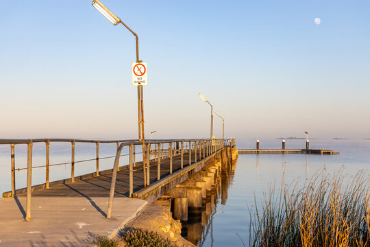 The moon setting over the jetty on a calm morning on the Coorong at Meningie South Australia on October 2nd 2023
