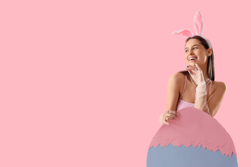 Sexy young woman in bunny ears with big paper Easter egg on pink background