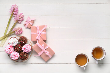 Plate with tasty cupcakes, presents, hyacinths and cups of tea on white wooden background