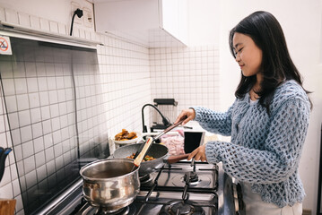 Young Asian woman standing by the stove in the kitchen and cooking