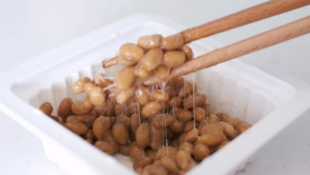 Wooden chopsticks holding Japanese natto beans on white background side view.