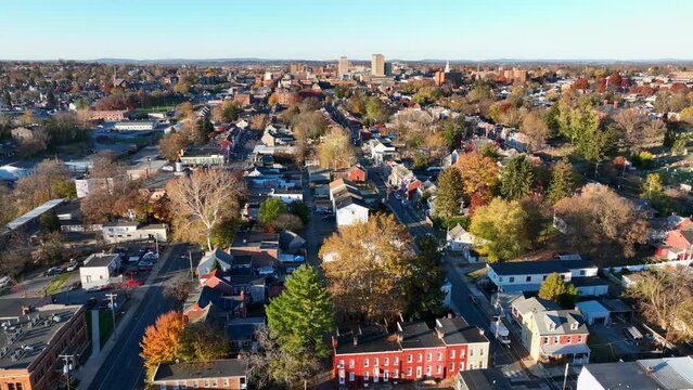 Small city in USA during autumn. Aerial orbit shot of suburb with colorful rowhouses and trees. Downtown city skyline view during sunset.