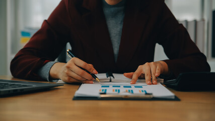 Asian Businesswoman Using laptop computer and working at office with calculator document on desk, doing planning analyzing the financial report, business plan investment, finance analysis concept.
