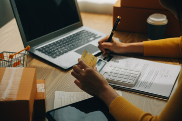 Young woman holding a smartphone, tablet showing payment success and credit card with yellow parcel box as online shopping concept in office