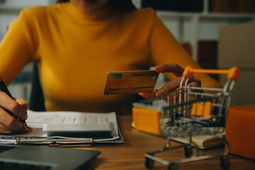 Young woman holding a smartphone, tablet showing payment success and credit card with yellow parcel box as online shopping concept in office