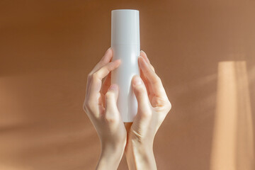 Cream tube on in women's hands on a brown background. Cosmetic skincare product blank plastic package. White unbranded lotion, balsam, toothpaste mockup. Sunscreen cream bottle with SPF