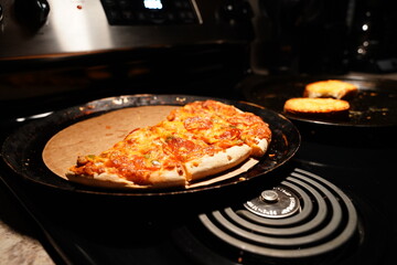A half-eaten supreme pizza sits on a stove.