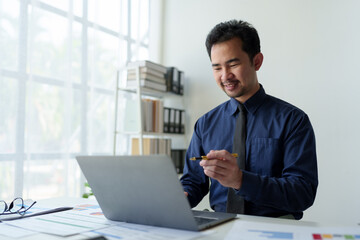 Asian businessman points at laptop computer screen to calculate budget, financial statistics and discuss financial services and management issues.