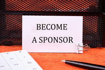 BECOME A SPONSOR text written on a white card next to the calculator, a pen on an orange background