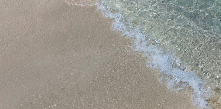 Gentle waves from a crystal clear sea wash ashore and break onto the pristine untouched sandy beach from the right. Widescreen image, copy space