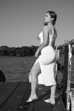 black dress, Latina with blue sky, and posing next to the lake, full body, face, posing at the dock, nice figure in black and white