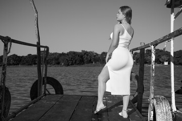 black dress, Latina with blue sky, and posing next to the lake, full body, face, posing at the dock, nice figure in black and white