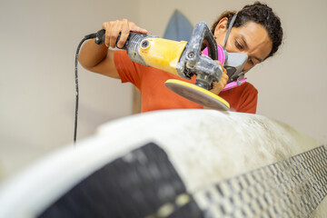 Man grinding the edges of a surfboard in a shop