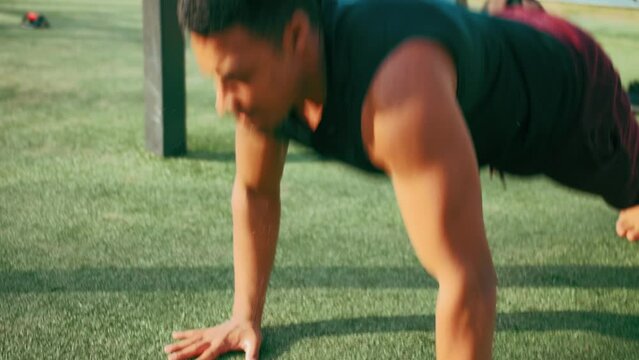 young mixed race male doing explosive push up jumps in outdoor callisthenics park