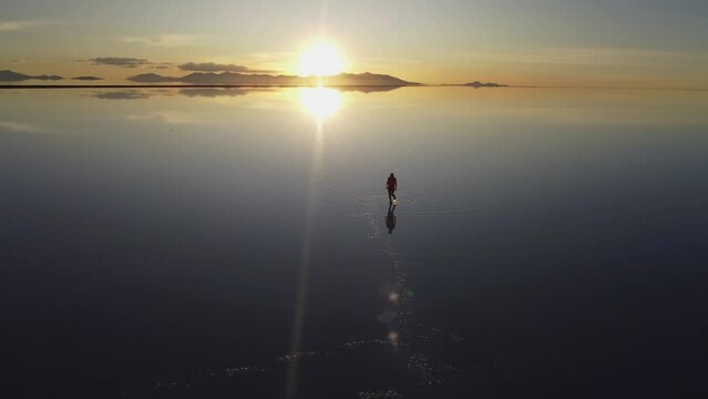 Woman walks on reflective lake surface, Uyuni salt flat sunset Bolivia