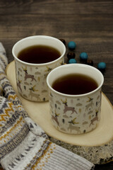 Two mugs with hot tea on a wooden background. Tea close-up during the cold season. Tea, a knitted sweater, and sweets create coziness. Poster for interior.