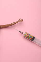 Drug addiction. Doll hand and syringe with sprinkles on a pink background. Party, medicine concept. Minimalism