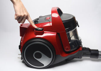 Finger presses the button of a red vacuum cleaner