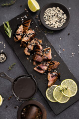 sliced pieces of Organic grilled Tuna Steak on black stone serving board and teriyaki soy sauce