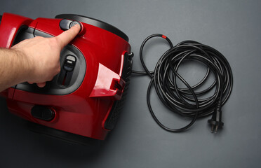 Finger presses the button for rewinding the electrical cable of a vacuum cleaner