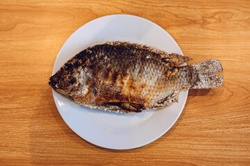 Grilled fish in a white plate with a wooden background.