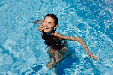 Happy woman swimming in pool in red swimsuit with loose long hair, skin protection with sunscreen, concept of relaxing on vacation.