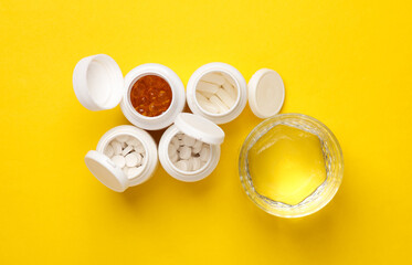 Different Pills in plastic bottles and water glass on yellow background. Medicine concept. Top view