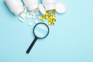 Different Pills in plastic bottles and magnifying glass on blue background. Medicine concept.