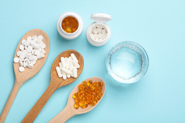 Pills in wooden spoons and glass of water on blue background