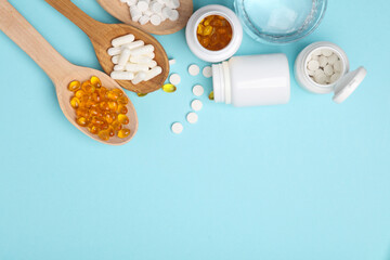 Pills in wooden spoons and glass of water on blue background