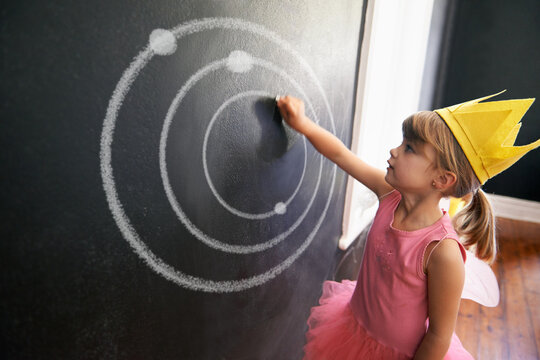 Child, board and drawing solar system for education with chalk in classroom with costume for creative, learning and guidance. Kid, chalkboard and crown for picture student in school for knowledge
