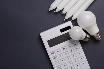 Alternatives lighting, savings. Calculator with led light bulb and wax candles on a dark background