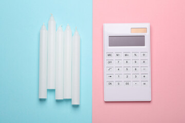 Calculator with wax candles on pink blue background. Savings, lighting costs