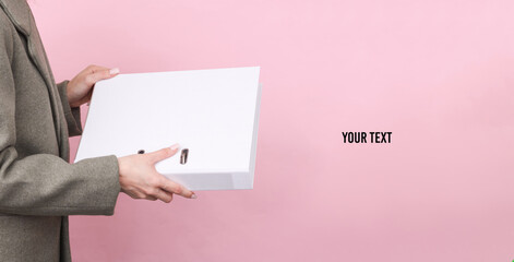 Business woman in a woolen coat holding white folder mockup on pink background. Space for your text