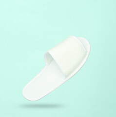 White hotel slippers levitating on a blue background with a shadow