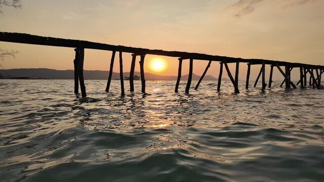 Old wooden pier silhouette against a tranquil ocean at sunset, evoking a serene, peaceful summer evening