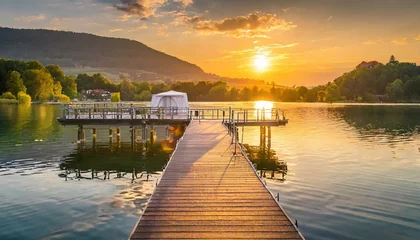 Tuinposter sunset over the lake wallpaper pier jetty golden hour sunset on lake, trees in background landscape © Ali