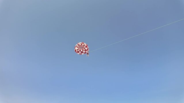 Parasailer soaring in a cloudless blue sky with a red and white striped parachute, showcasing leisure and extreme sports during summer holidays
