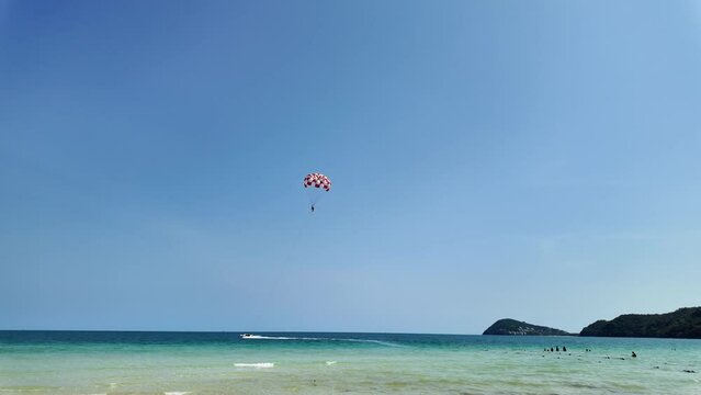 Tropical beach scene with vibrant blue skies, crystal-clear water, and a person parasailing with a red and white parachute, evoking a sense of adventure and leisure in summer holidays