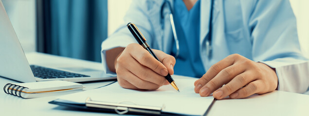 Doctor at hospital sit at his desk working on paperwork diagnosing patient test results, developing...