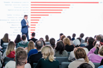 Audience engaged at a business conference with a male speaker presenting financial performance.