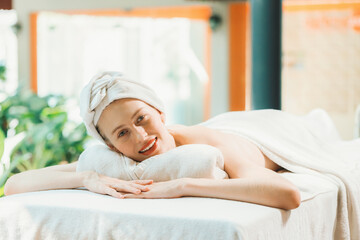 Obraz na płótnie Canvas Beautiful young woman relaxes on a spa bed surrounded by nature. ready for a body massage. Attractive female in white towel lying peacefully during waiting for body massage. Close up. Tranquility