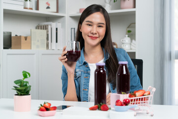 Smiling young beautiful Asian reviewing tasty mixed strawberry and cherry juice detox drinks,...