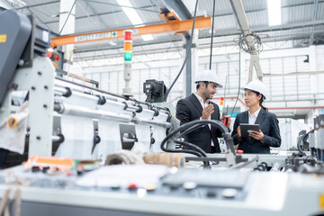 European male engineer and Asian female senior official Owners and business partners of industrial plants Wear a suit to talk and inspect the operation of plastic and steel export production machinery - obrazy, fototapety, plakaty