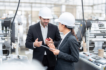 European male architectural engineers and senior officials Asian woman Analyze machinery systems and view projects via tablet. Wear a suit and safety helmet in the material manufacturing industry.