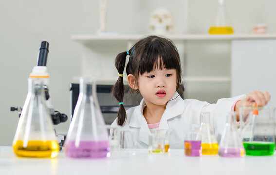 Asian little cute girl students in lab coat making test tube science experiments chemical laboratory in study room at school. Education research and development concept learning kids.