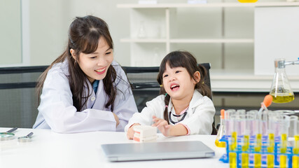 Asian woman doctor physiotherapist explains human fake skeleton teeth model on a table to little cute children girl at laboratory study room. Education anatomical human concept learning for kids.