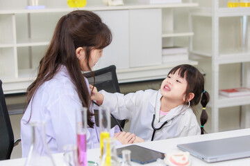 Fototapeta premium Asian woman doctor and cheerful little girl applying medical stethoscope at doctor appointments in laboratory lab. Education healthcare, medicine childrens hospital concept learning for kids
