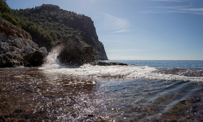 Panoramic view of the mountain and splashes of waves at the rocky coast of the Mediterranean Sea in good sunny weather in February in Alanya Turkey.