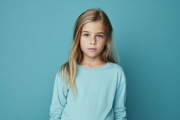 Fototapeta premium Little girl with long blonde hair looking at camera over blue background